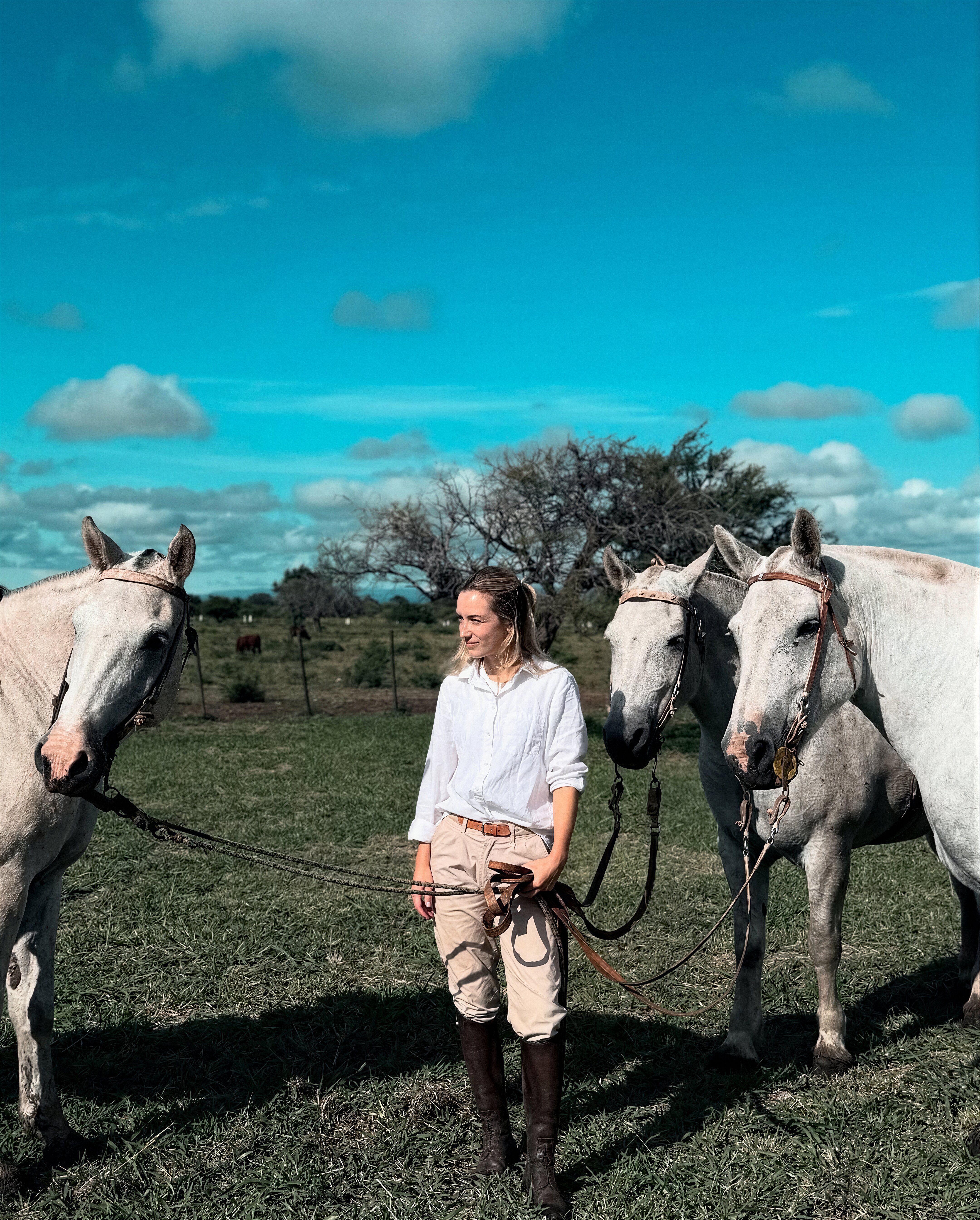 Rider standing with two white horses on the open pampas